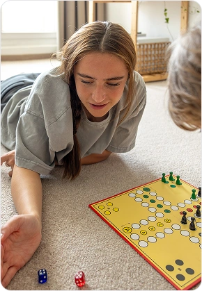 Twee kinderen spelen een strategisch bordspel thuis met dobbelstenen en pionnen.